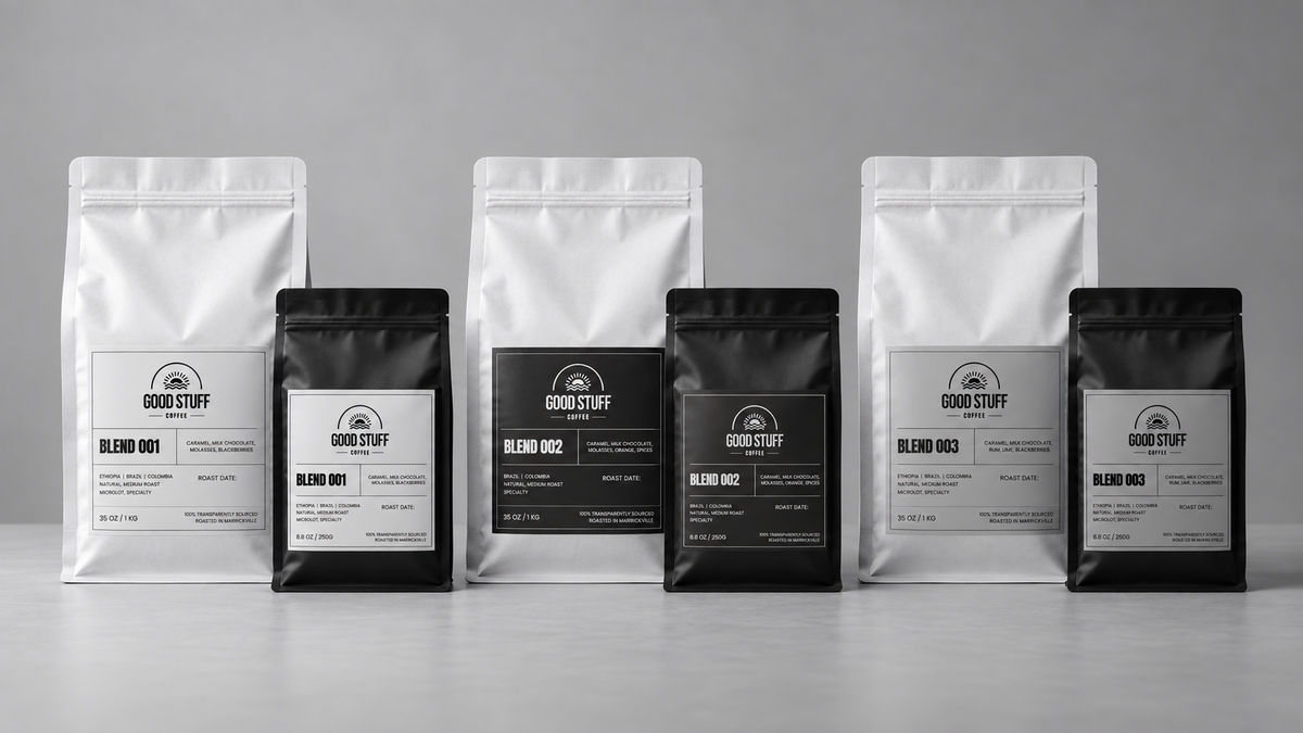 Six coffee bags from Good Stuff are arranged in a row on a light gray surface against a neutral gray background. The set includes three white stand-up pouches and three black stand-up pouches, each with a minimalist label showing the Good Stuff logo and the blend name Blind 800.